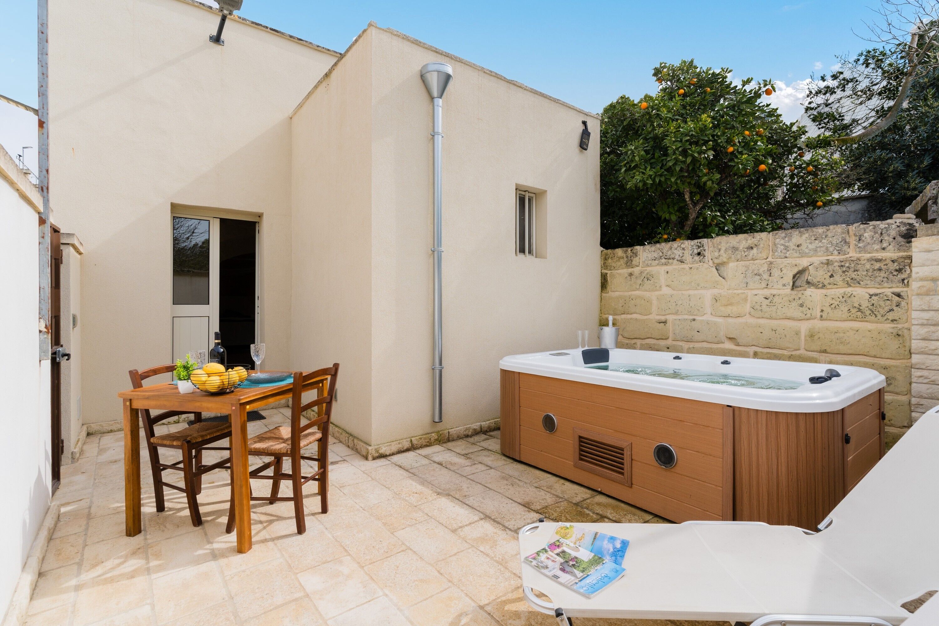 A patio with a wooden table, a hot tub, and a lounge chair.