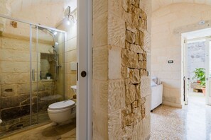 Une salle de bain avec une douche à parois de verre, des toilettes et un mur en pierre.