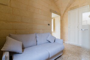 Una habitación con un sofá de tonos claros, una puerta blanca y una pared de piedra.