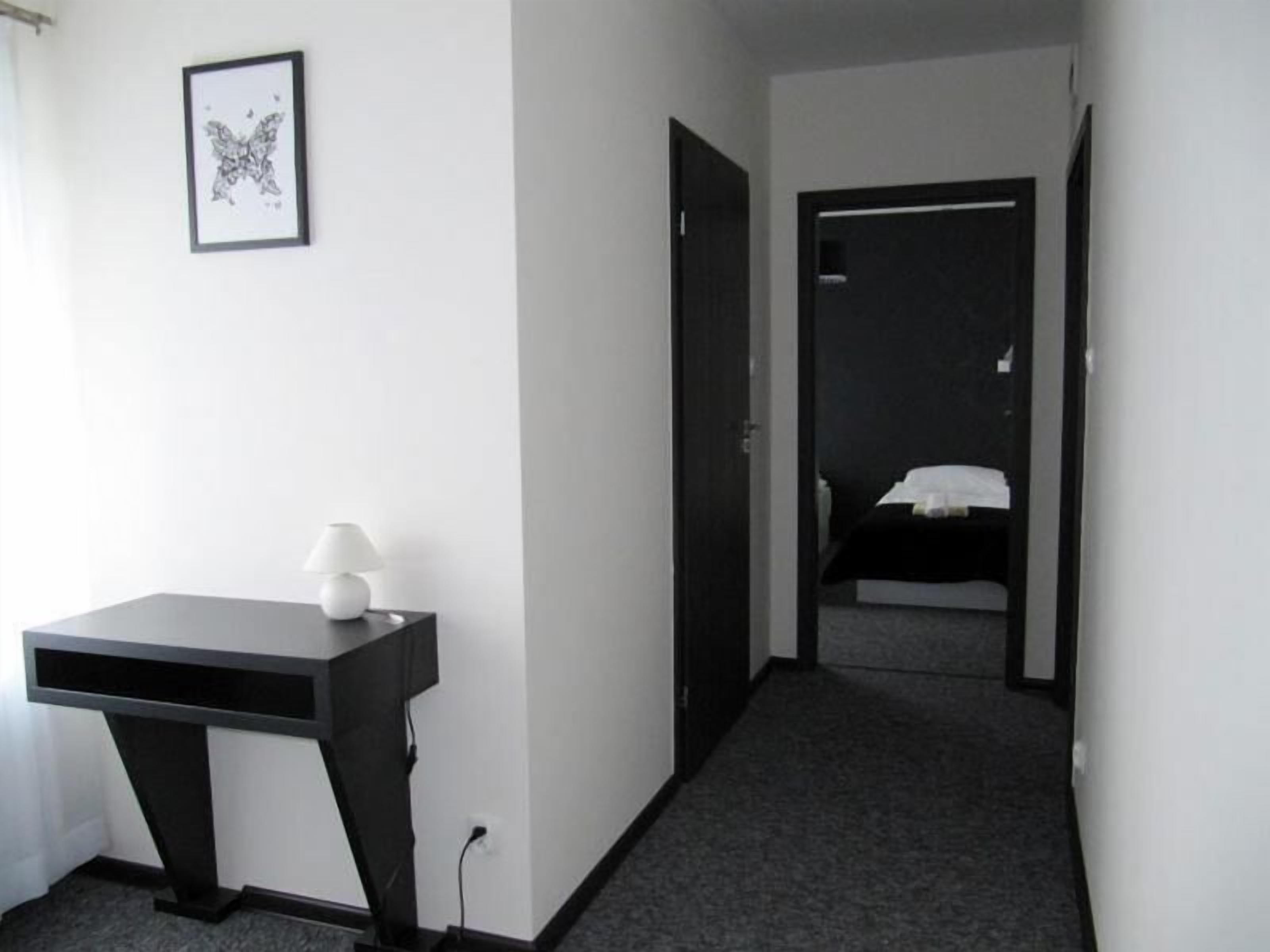 A hotel room with a desk, a lamp, a framed picture on the wall, and a bed in the background.