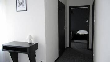 A hotel room with a desk, a lamp, a framed picture on the wall, and a bed in the background.