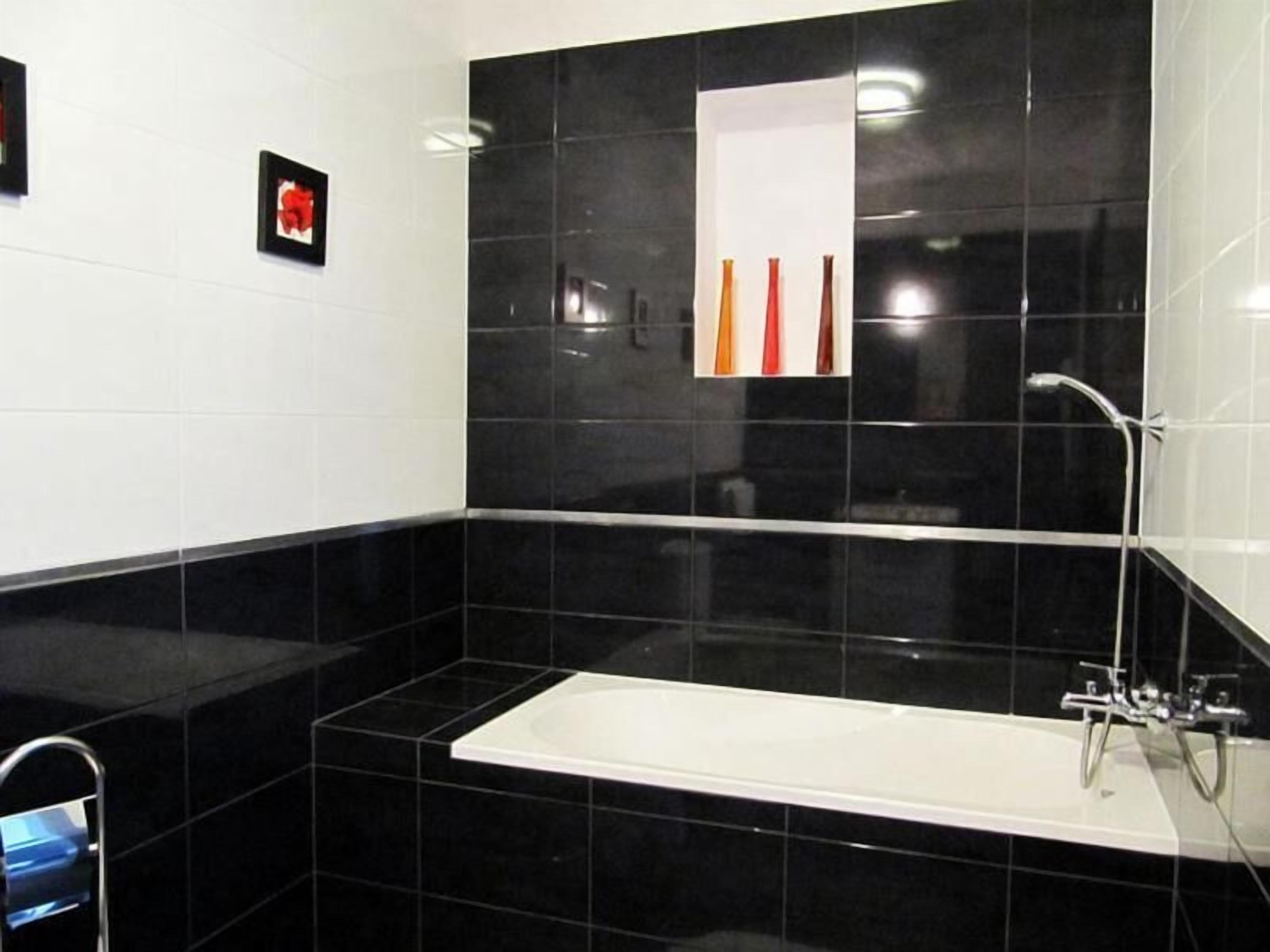 A modern bathroom with black tiles, a white bathtub, and a shower area.