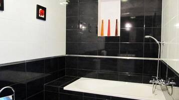 A modern bathroom with black tiles, a white bathtub, and a shower area.