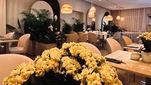 Un comedor con mesas redondas, sillas, lámparas colgantes y plantas en macetas.