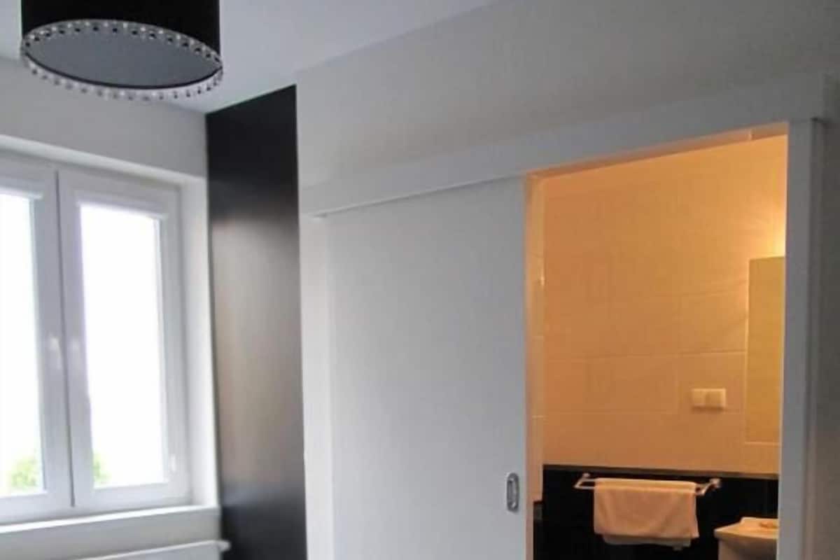 Un dormitorio con cama, ventana y puerta que da a un baño con inodoro y lavabo.