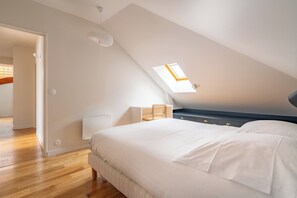 Ein Schlafzimmer mit schrägem Dach, Oberlicht, Bett, Nachttisch und Sessel.
