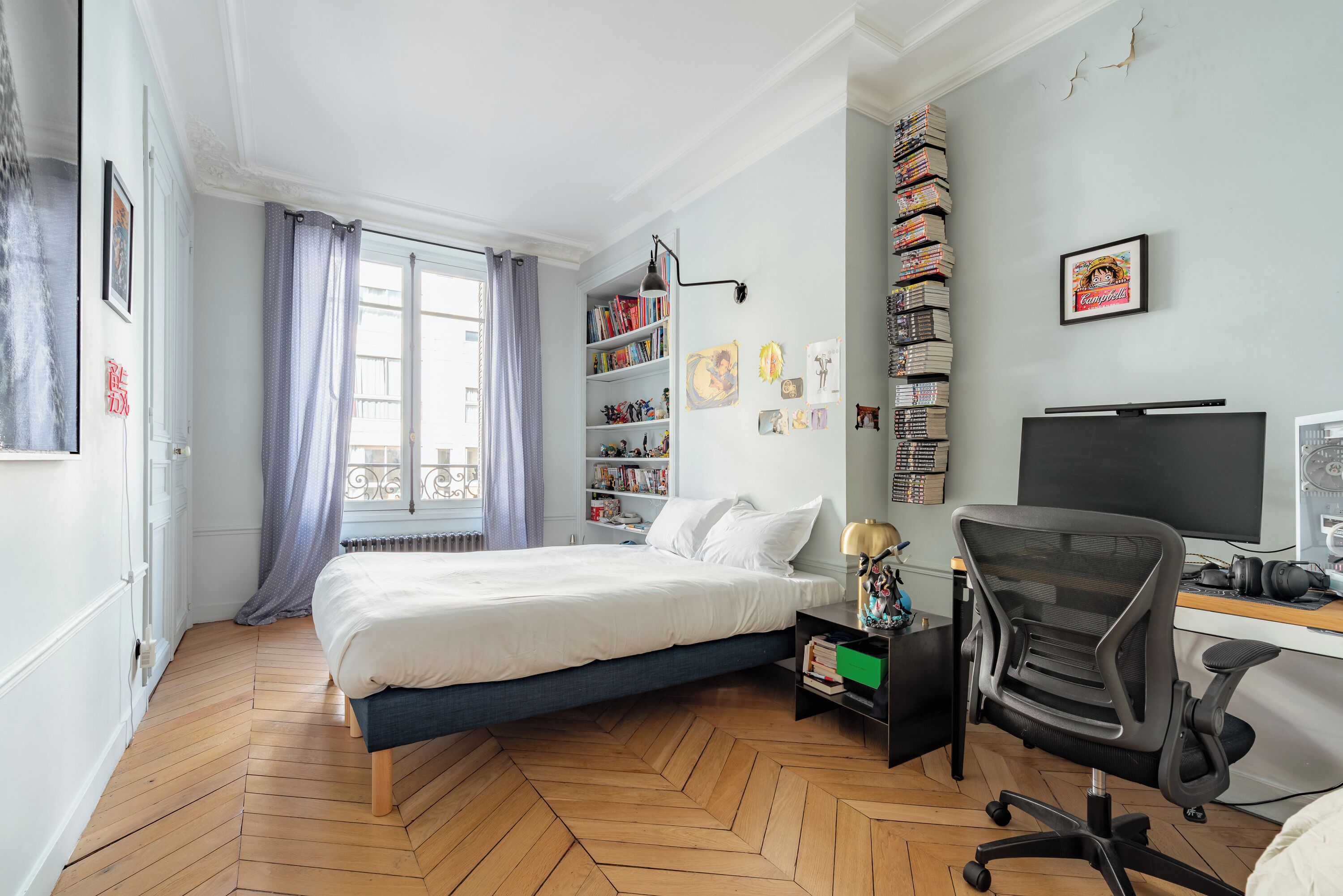 Quarto com cama, escrivaninha com computador, cadeira, estante de livros e janela com cortinas.