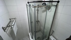 Cabina de ducha con paredes de vidrio, un cabezal de ducha manual, un perchero y un inodoro.
