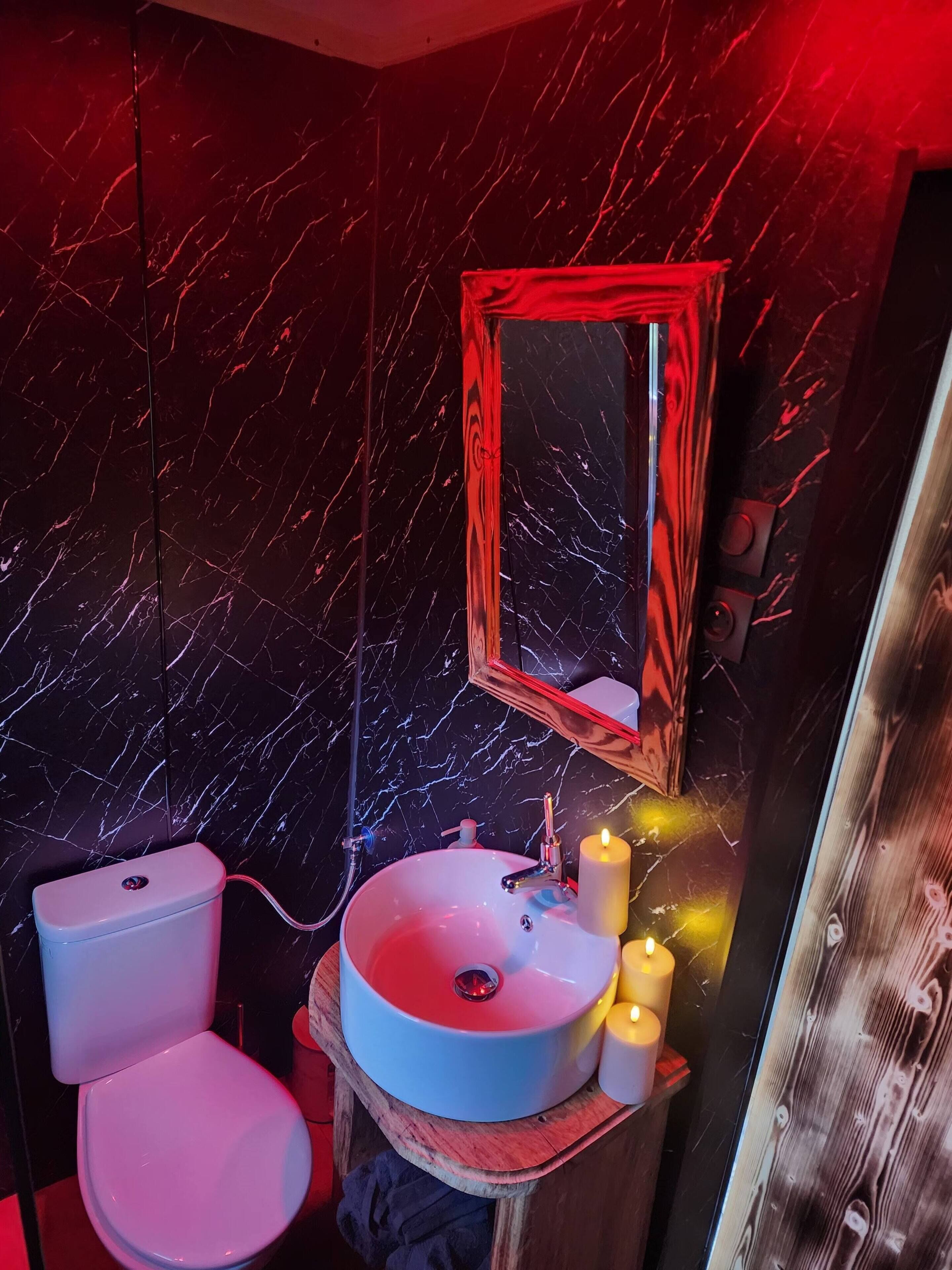 A bathroom with a marble wall, a toilet, a sink with a mirror, and candles.