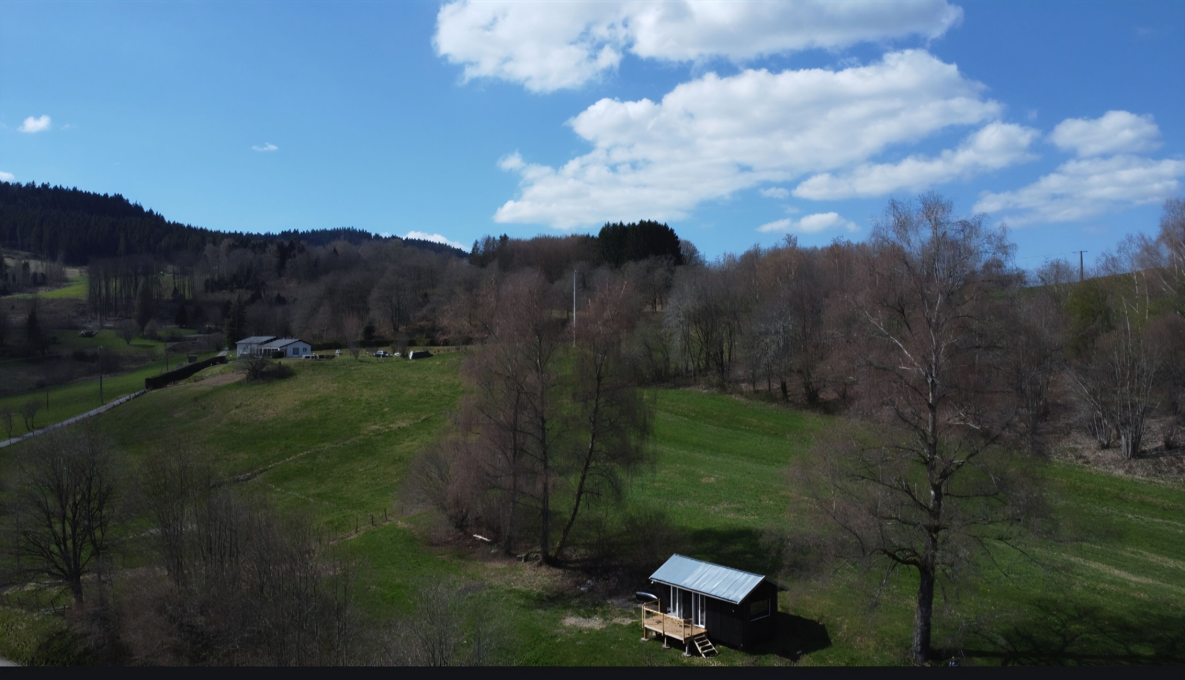 A rural landscape with a small house, open fields, and a forested hill in the background.