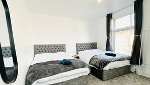 A bedroom with two beds, a large mirror, and a window with curtains.