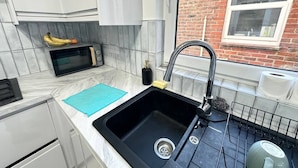 A compact kitchen with a black sink, a microwave, and a dish rack.