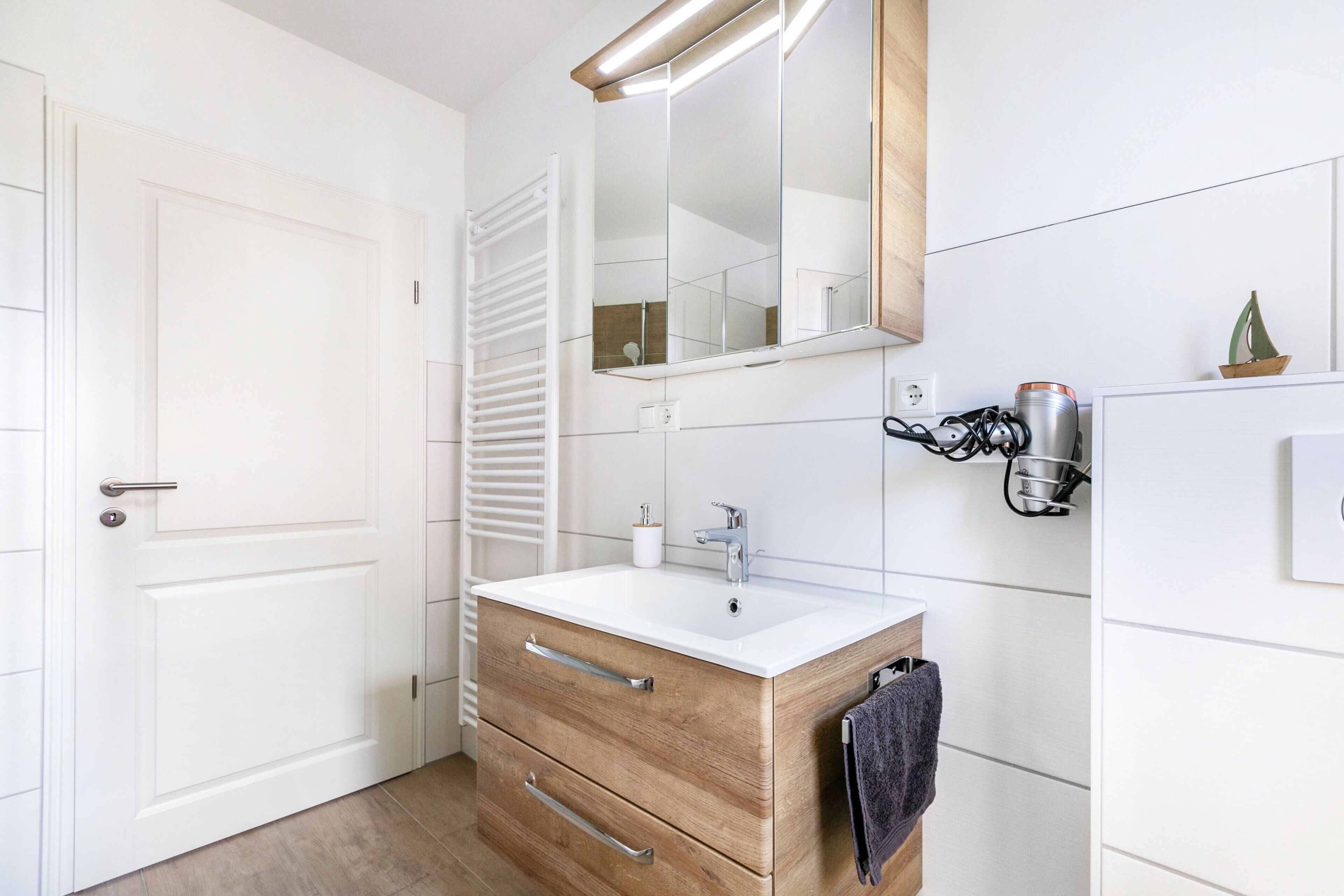 Une salle de bain avec un lavabo blanc, un meuble-lavabo en bois, un porte-serviettes, un miroir et une serviette accrochée au mur.