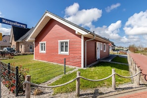 En rød bygning med en hvid dør og vinduer, omgivet af en grussti og et rebhegn.