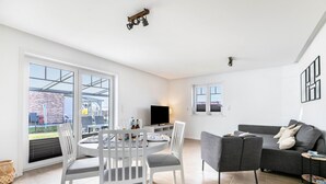 Una sala de estar moderna con comedor, un sofá gris y un televisor.