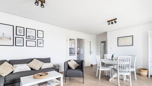 Una sala moderna con un sofá gris, una mesa de centro blanca y un comedor con sillas blancas.