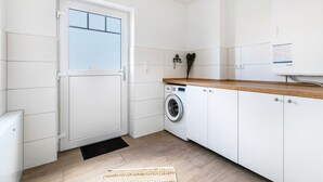 Un cuarto de lavandería con lavadora, armarios, una encimera de madera y una puerta con ventana.