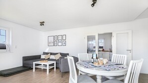 Una sala moderna con un sofá gris, una mesa de centro blanca y una mesa de comedor con sillas blancas.