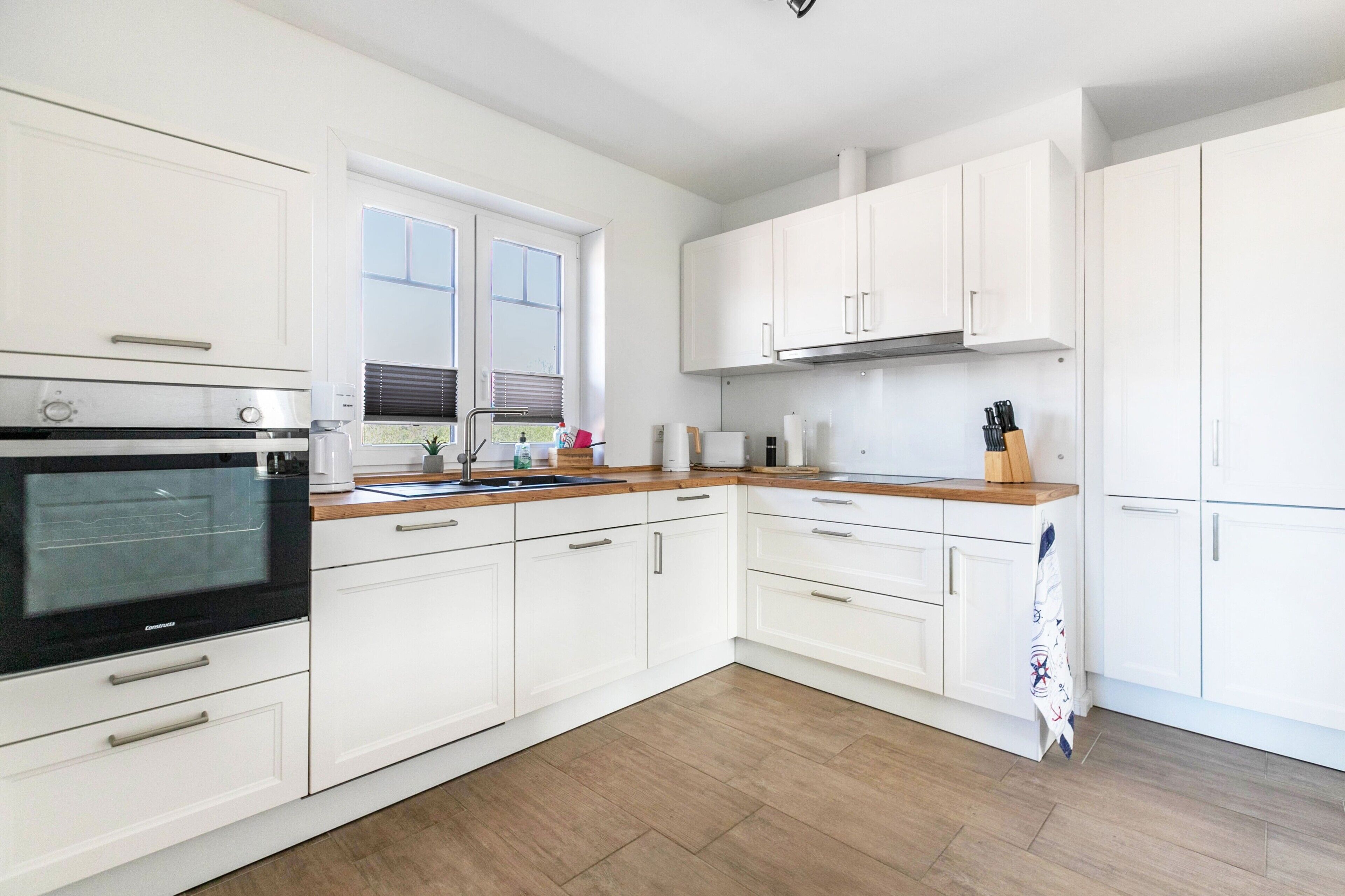 Eine moderne Küche mit weißen Schränken, einer Holz Arbeitsplatte und einem eingebauten Backofen.