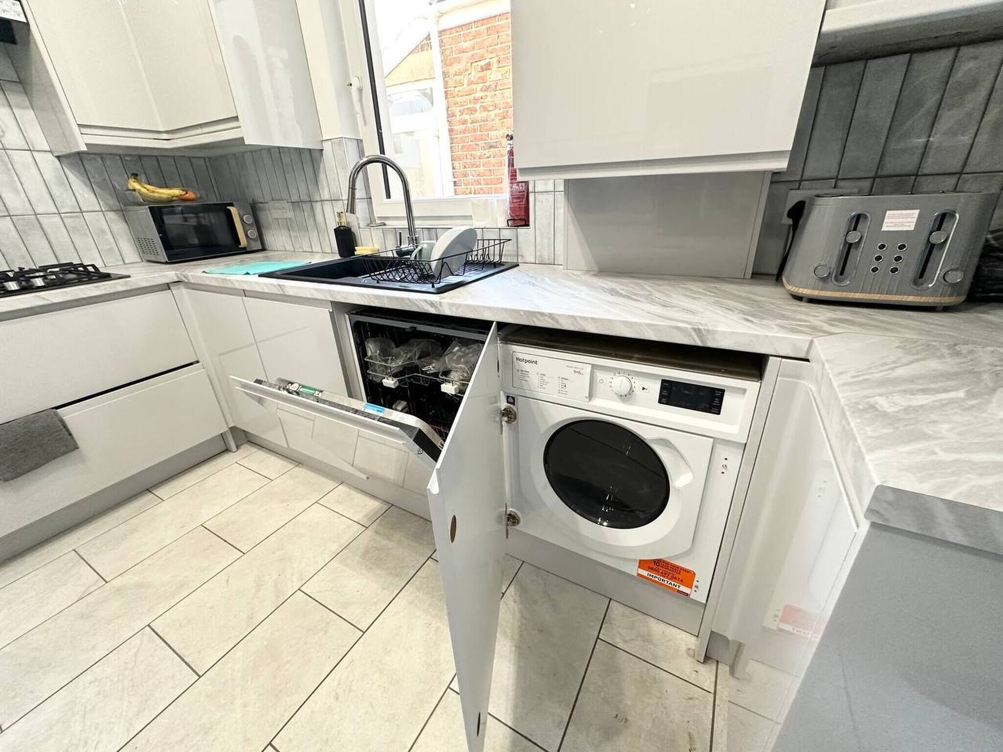 Een compacte keuken met een ingebouwde wasmachine, een magnetron en een gasfornuis.