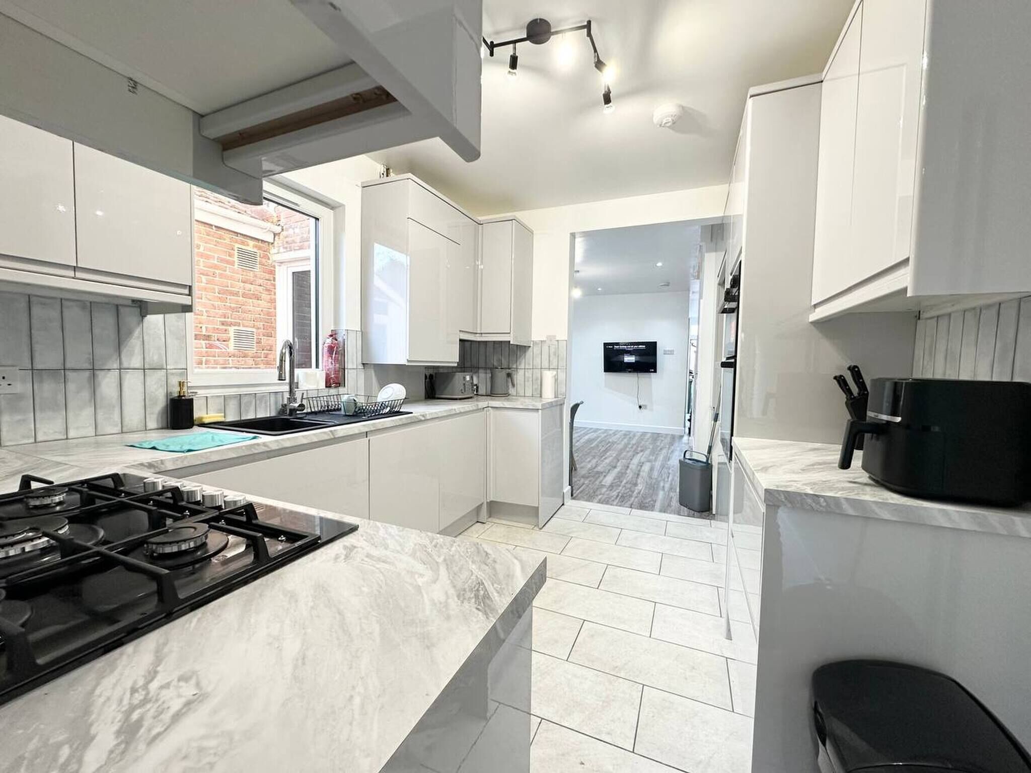 A modern kitchen with white cabinets, a gas stove, and a TV mounted on the wall.