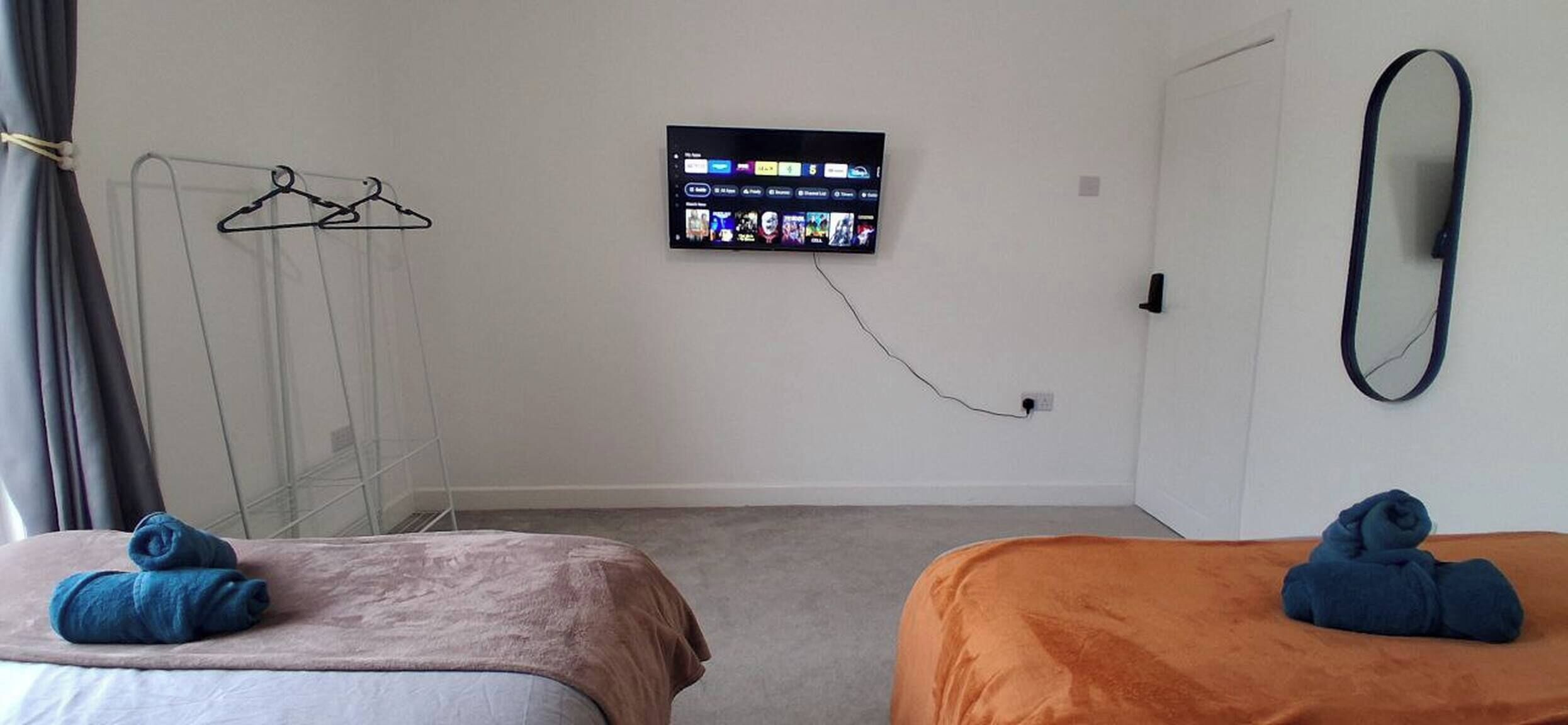 Een hotelkamer met twee bedden, een aan de muur bevestigde televisie, een spiegel en een kledingrek.