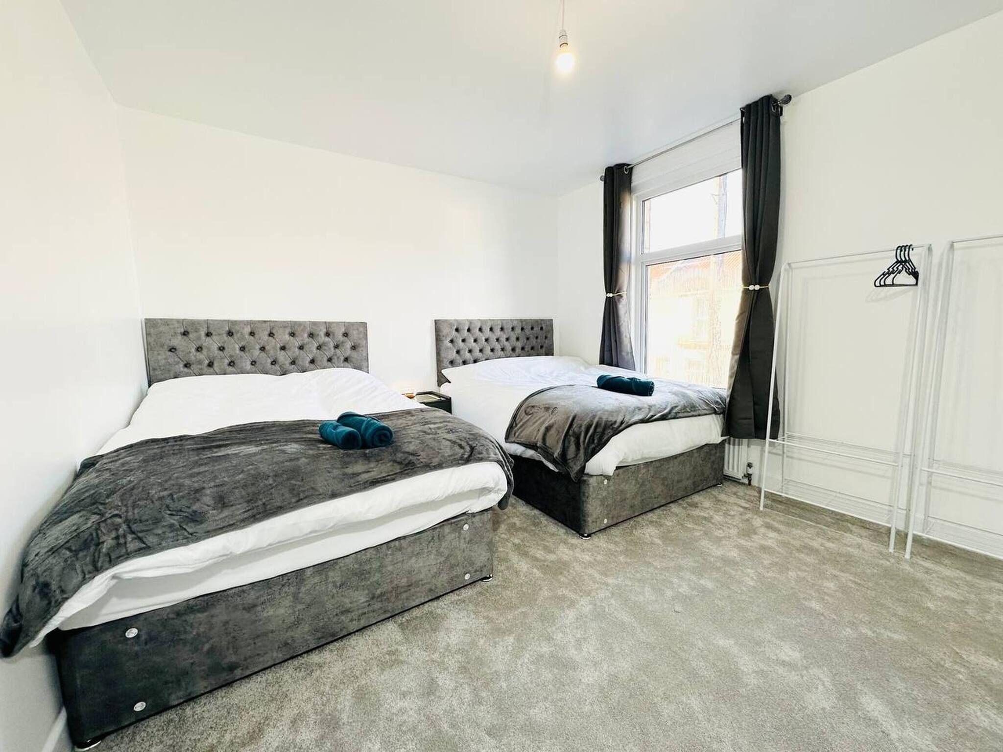 A bedroom with two beds, a window with curtains, a hanging light fixture, and a wardrobe.