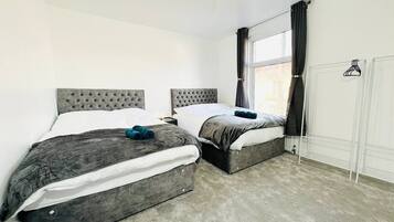 A bedroom with two beds, a window with curtains, a hanging light fixture, and a wardrobe.