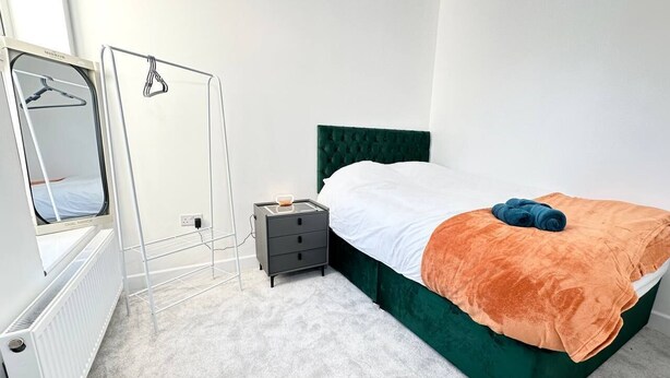 A bedroom with a bed, a nightstand, a radiator, and a wardrobe.