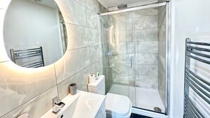 A modern bathroom with a glass-enclosed shower, a round mirror, and a white sink.