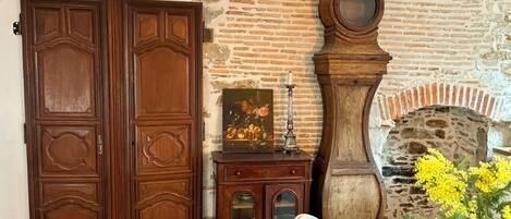 A room with a wooden wardrobe, a cabinet with glass doors, a wall clock, and a fireplace.