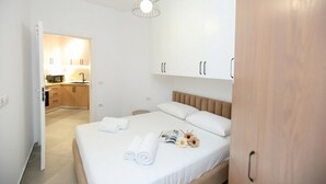A modern hotel room with a bed, a bedside table, a wardrobe, and a kitchenette in the background. - Halina (Orikum)
