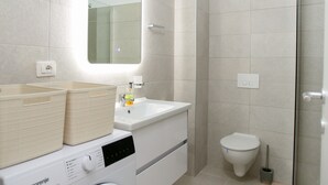 A modern bathroom with a washing machine, a sink, a toilet, and a shower area. - Halina (Orikum)