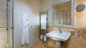 Un baño con cabina de ducha de vidrio, un lavabo blanco, un perchero con toallas y un espejo grande.