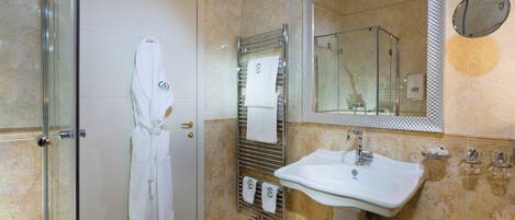 A bathroom with a glass shower enclosure, a white sink, a towel rack with towels, and a large mirror.