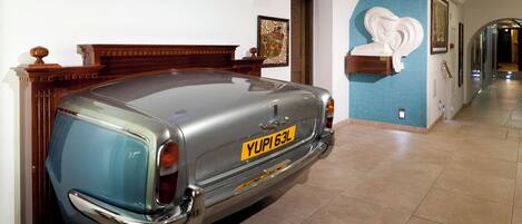A vintage car parked in a hallway with a blue wall and a white sculpture.