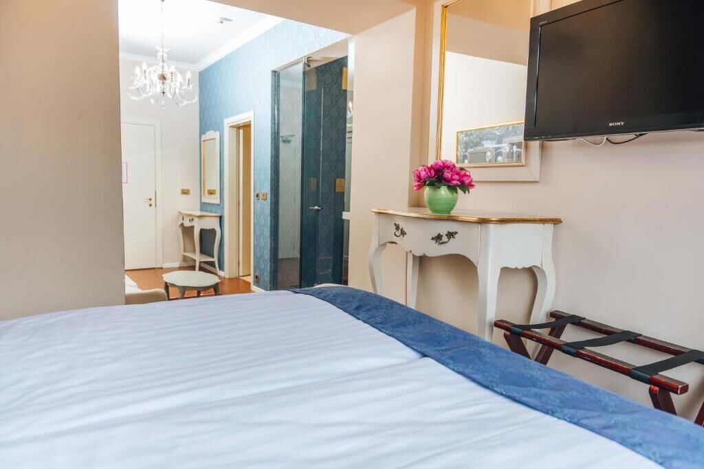 A bedroom with a bed, a dresser, a TV, a mirror, and a door leading to a bathroom.