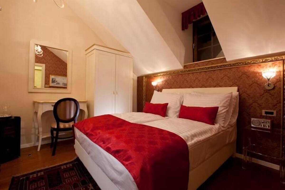 A bedroom with a bed, a desk, a chair, a mirror, and a small table with a radio.