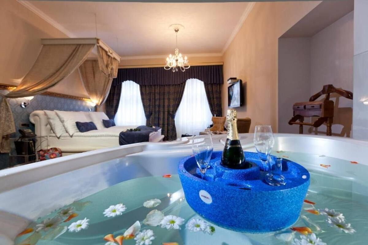 A bedroom with a large bed, a sitting area, a TV, and a hot tub with flowers.