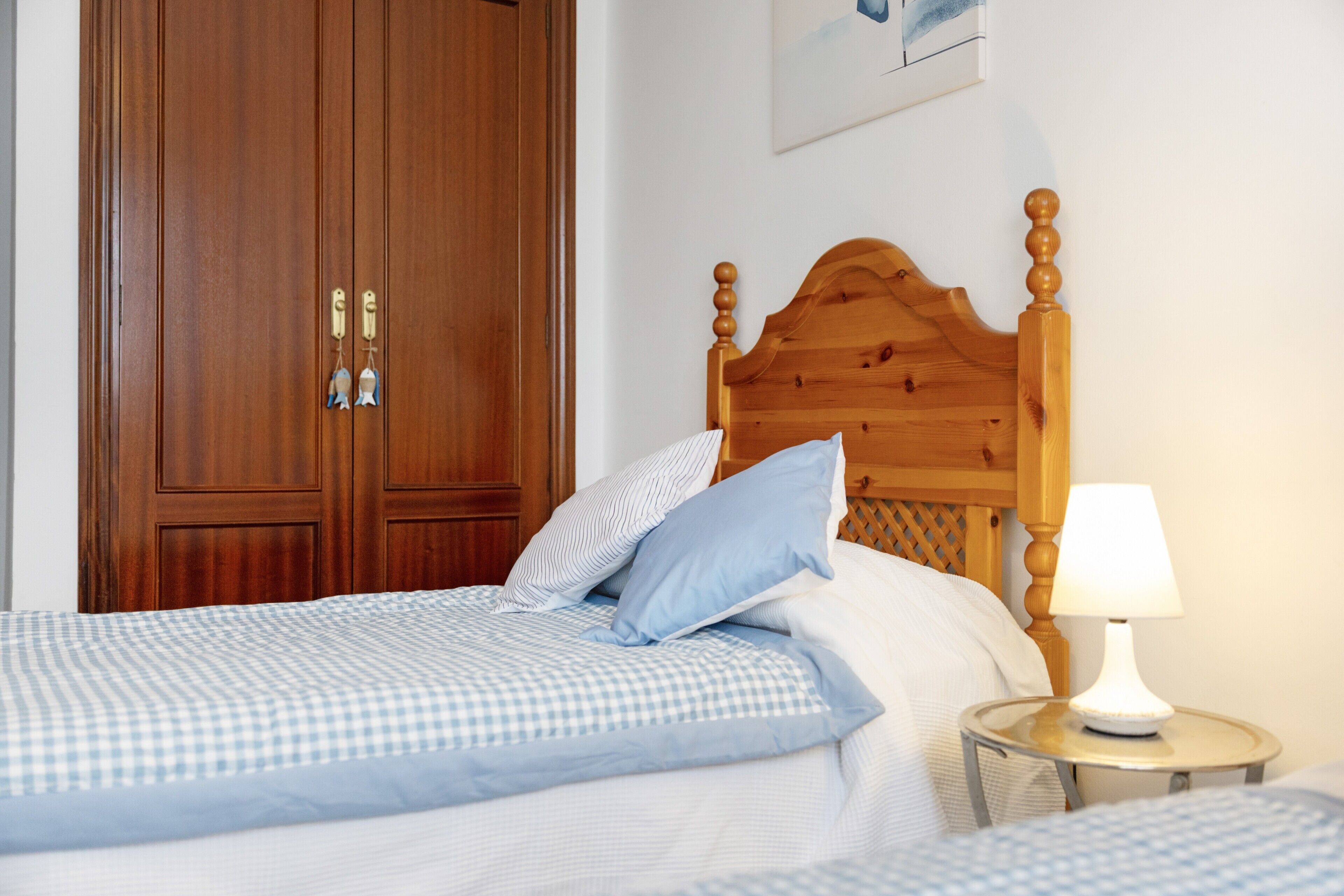 Een slaapkamer met een houten hoofdbord, een nachtkastje met een lamp en een geruit beddegoed.