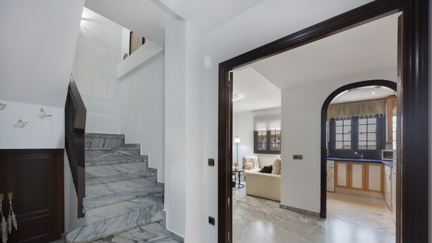 A marble staircase leading to a living area with a sofa and a kitchen in the background. - Vacation Apartment 9 min from Bajo de Guía with Shared Terrace, Wi-Fi & Air Conditioning (Sanlúcar de Barrameda)