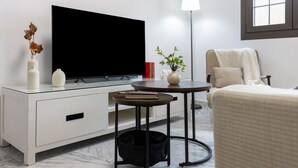 A modern living room with a flat-screen TV, a white cabinet, a small round table, a floor lamp, and a comfortable chair. - Vacation Apartment 9 min from Bajo de Guía with Shared Terrace, Wi-Fi & Air Conditioning (Sanlúcar de Barrameda)