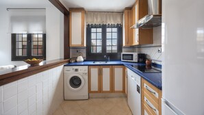A compact kitchen with a washing machine, microwave, and wooden cabinets. - Vacation Apartment 9 min from Bajo de Guía with Shared Terrace, Wi-Fi & Air Conditioning (Sanlúcar de Barrameda)