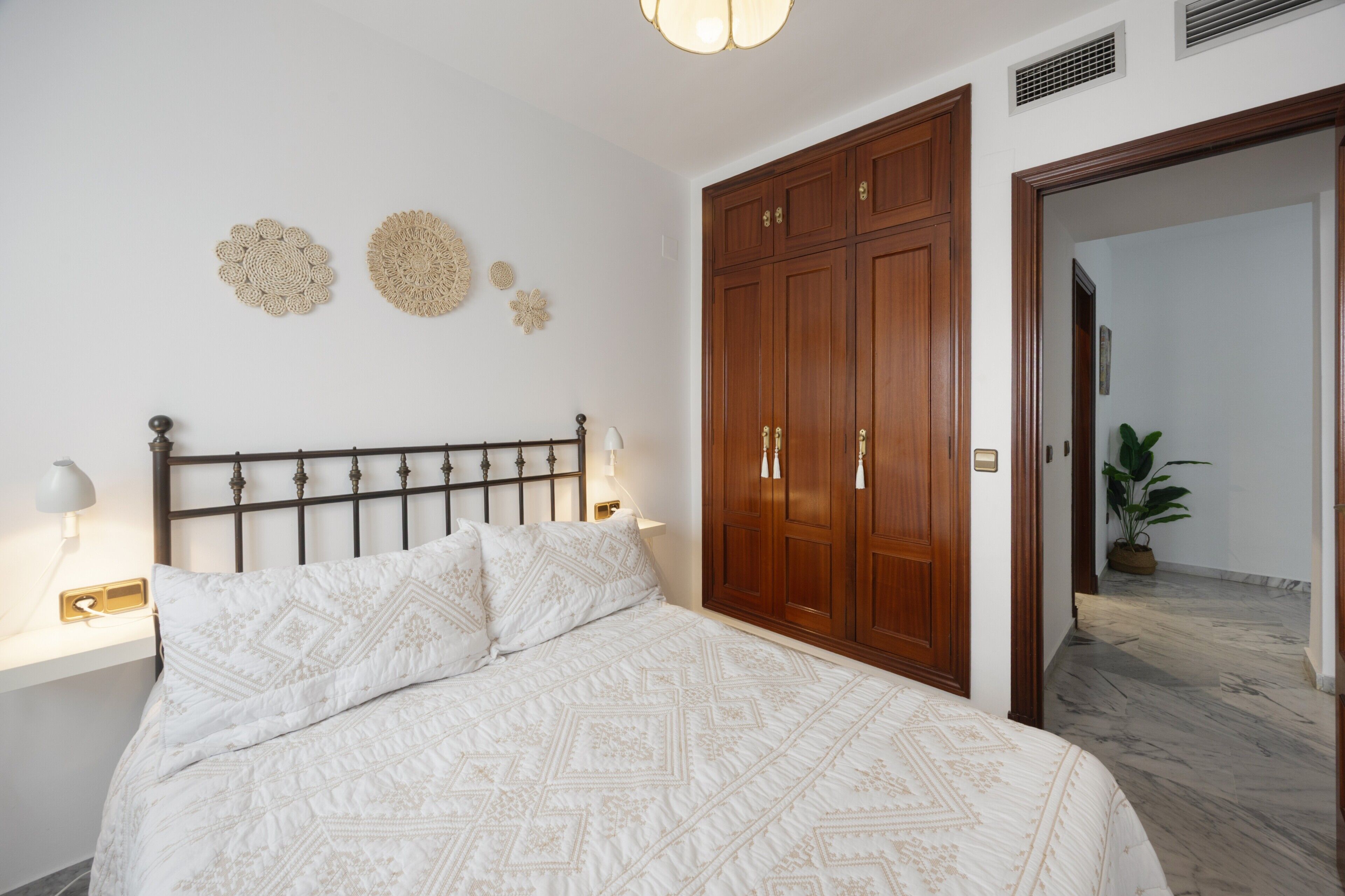 Une chambre à coucher comprenant un lit, des lampes de chevet, une armoire en bois et des œuvres d’art décoratives accrochées au mur.
