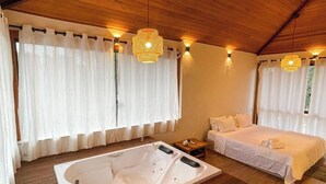 Une pièce avec un plafond en bois, un grand lit, un espace nuit séparé, une baignoire et deux lampes suspendues.