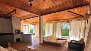 Un espace intérieur spacieux avec un plafond en bois, un coin salon avec des coussins, une table à manger et une plante en pot.