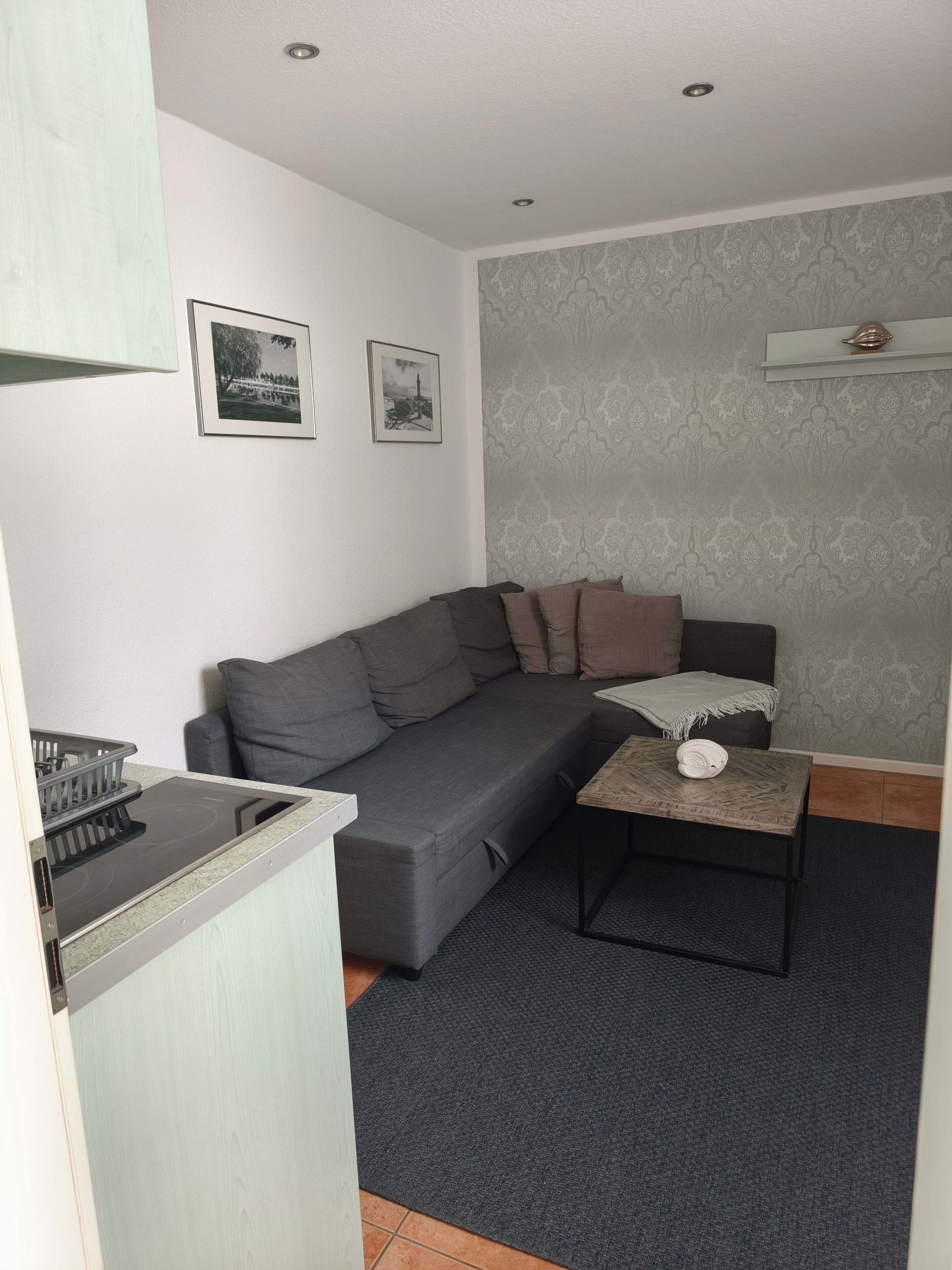 A modern living room with a grey sofa, a small coffee table, and a kitchen area with a stove.