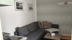 Ein modernes Wohnzimmer mit einem grauen Sofa, einem kleinen Couchtisch und einer Küchenzeile mit Herd.
