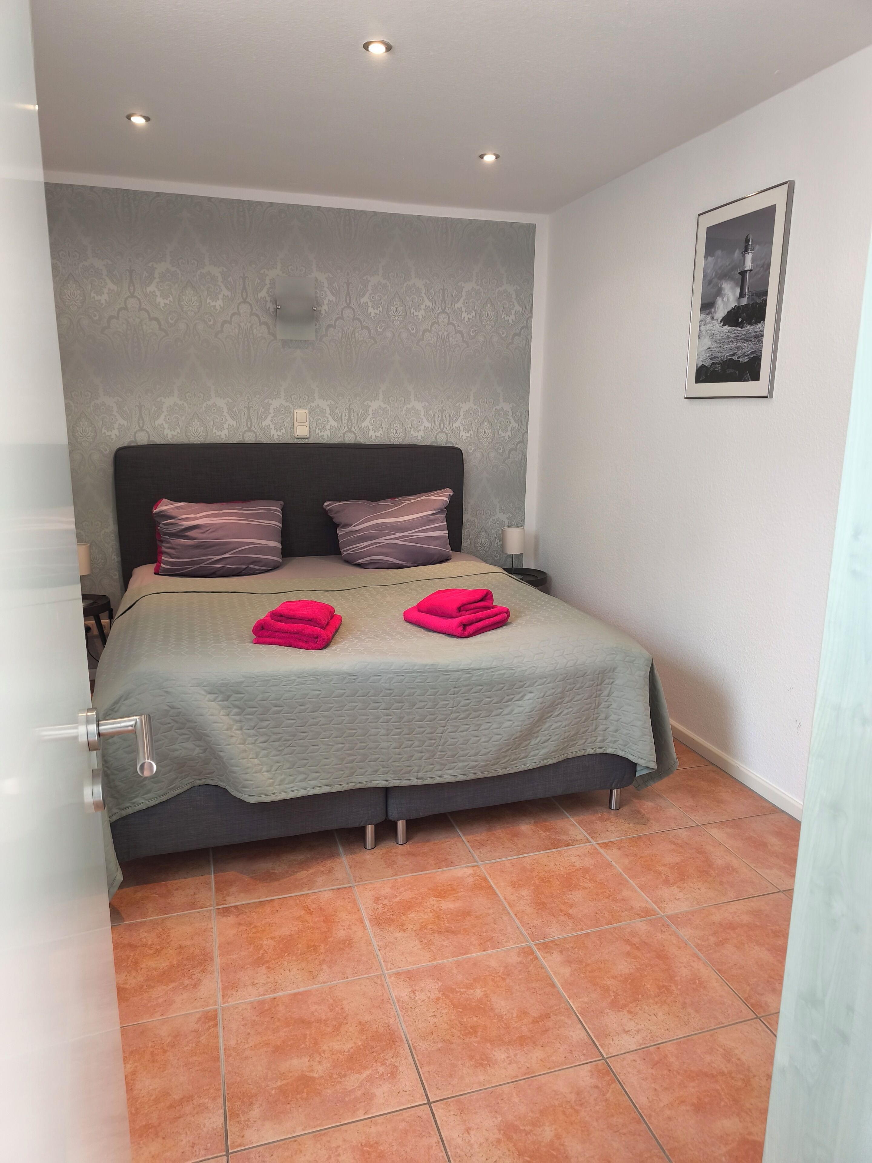 Une chambre à coucher avec un lit, deux oreillers, une table de chevet, un tableau accroché au mur et une porte.