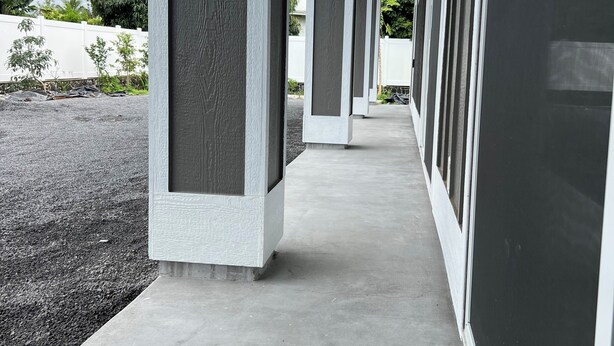 A covered walkway with concrete pillars and a flat roof, leading to a building with large windows. - Spacious 4-bedroom , newly building in center of Hilo. (Hilo)